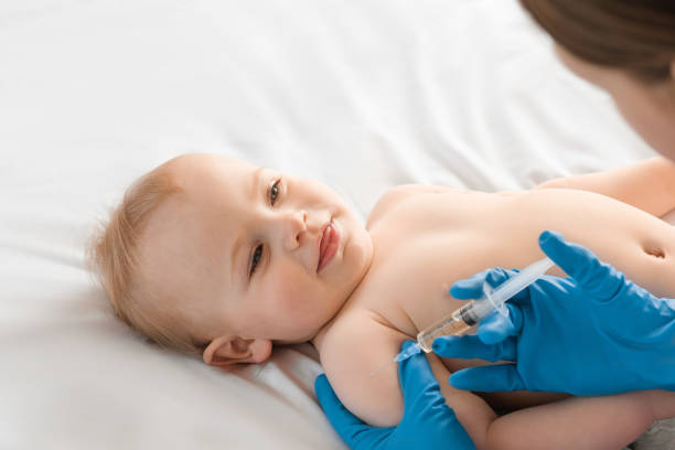 médico vacinando bebê sorridente na clínica. um ano bebê pequeno receber uma injeção. pediatra e paciente recém-nascido. vacina para criança recém-nascida. imunização infantil, vacinação, conceito de saúde - newborn little girls baby lying down - fotografias e filmes do acervo