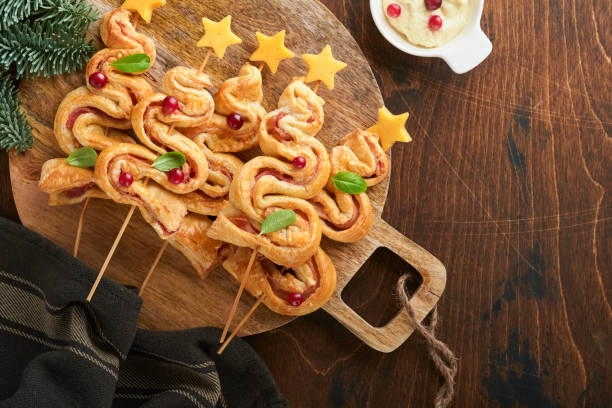 istock Christmas or New Year appetizer. Christmas tree shape puff pastry buns with cheese and ham. Group of Christmas tree shapes on wooden board. Festive idea for Christmas or New Year dinner. Top view. 1459678948