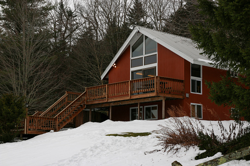 West Dover, Vermont, USA - 31 December 2022: A classic A-Frame Ski vacation home with a wood deck and staircase with snow on the ground available to rent.
