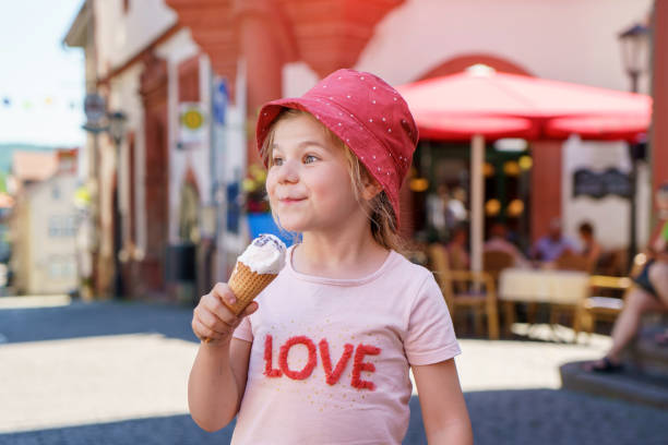 Beautiful little girl eats ice-cream in the summer. Happy funny preschool girl with sweet ice cream cone in the city. Beautiful little girl eats ice-cream in the summer. Happy funny preschool girl with sweet ice cream cone in the city licking ice cream cone stock pictures, royalty-free photos & images