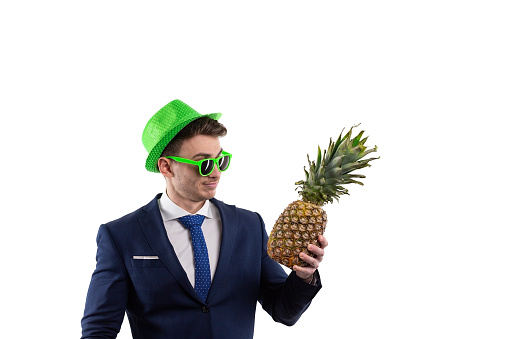A male businessman in a suit in cheerful green glasses and a hat holds a ripe pineapple in his hand rejoices and dances. The concept of the end of the working day, or the beginning of vacation corporate joy. High quality FullHD footage
