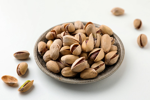 Plate and pistachio nuts on white background