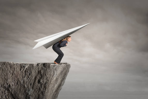 Businesswoman Standing At Edge Of Cliff Ready For Takeoff With A Paper Airplane stock photo