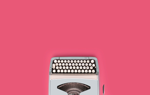 Overhead top view of a vintage aqua blue typewriter against a pink background.
