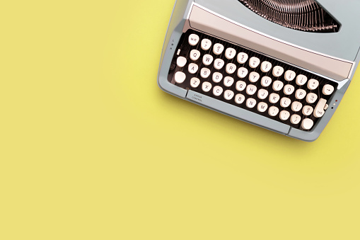 Overhead top view of a vintage aqua blue typewriter against a yellow background.