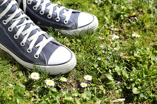 Person in stylish gumshoes standing on grass near beautiful blooming flowers, closeup