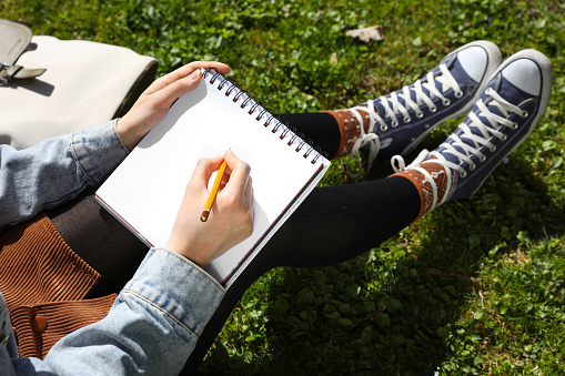 Woman drawing in sketchbook outdoors on green grass, closeup