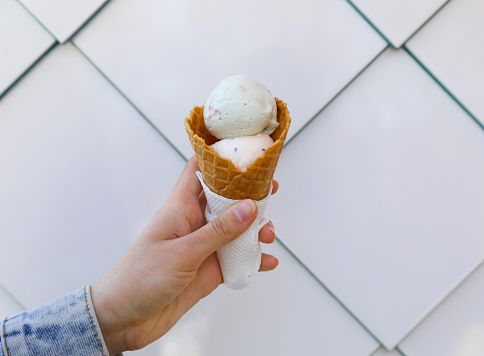 Woman holding delicious ice cream in waffle cone near white wall, closeup. Space for text