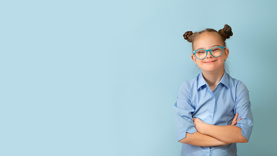 Happy girl with Down syndrome. Having fun, laughing. Funny pigtails. Studio. Portrait on a blue background
