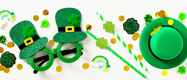 St Patrick's Day banner. Flat lay party glasses, drinking straws, leprechauns hat, confetti on white background.