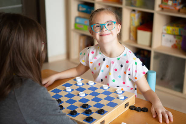 ragazza con la sindrome di down che gioca a dama - concentration chess playing playful foto e immagini stock