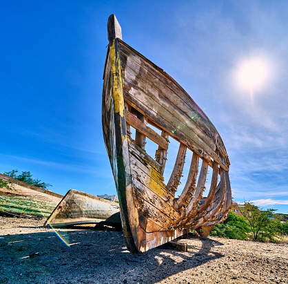 A closeup shot of an old broken boat on the coast against a blue sky.