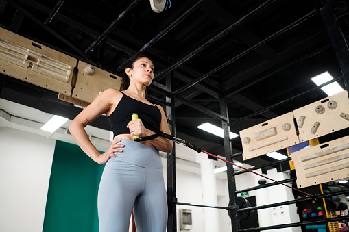 A latin woman standing in a gym and using the sports equipment.
