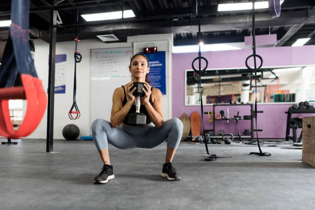 Young woman doing squat and holding dumbbell