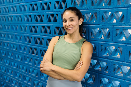 A happy fitness woman standing leaning on the wall with arms crossed and smiling at the camera.