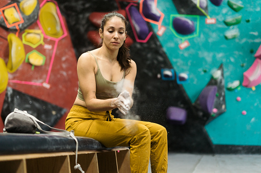 A young latin woman getting ready for bouldering and putting climbing chalk in her hands.