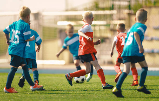 partido de fútbol entre niños. los escolares juegan al partido de fútbol con camisetas rojas y azules - soccer child coach childhood fotografías e imágenes de stock