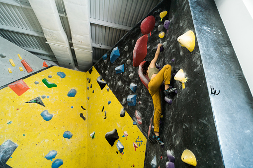 A latin female climber doing bouldering in an indoor rock climbing gym.