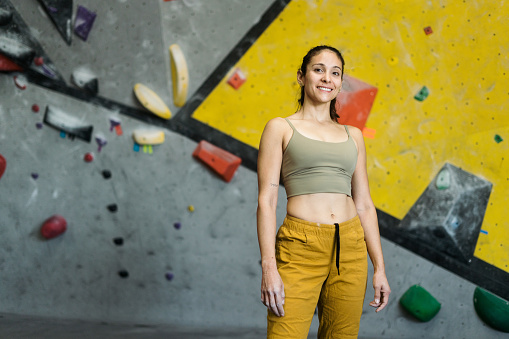 A beautiful latin young woman standing in a climbing gym and smiling at the camera.