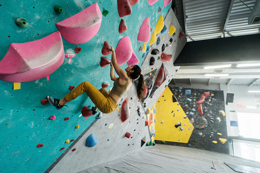 A latin female climber climbing a wall in an indoor gym.