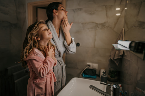 Mother and her little daughter doing evening routine, cleaning their faces in domestic bathroom.