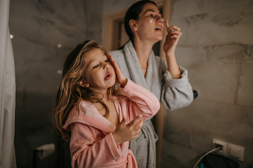 Mother and her little daughter doing evening routine, cleaning their faces with cream in domestic bathroom.