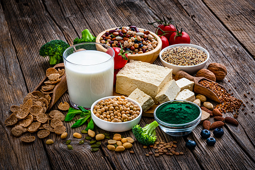 Group of healthy vegan food with high proteins content. The composition includes soy milk, tofu, soybean, spirulina, breakfast cereal, peanuts, almonds, walnut, pistachio, legumes, chia seeds, quinoa, broccoli, pumpkin seeds among others. High resolution 42Mp studio digital capture taken with SONY A7rII and Zeiss Batis 40mm F2.0 CF lens