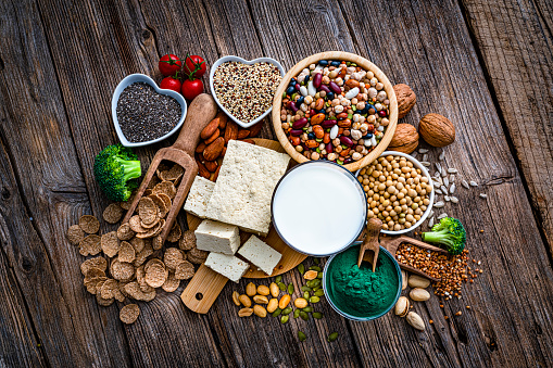 Overhead group of healthy vegan food with high proteins content. The composition includes soy milk, tofu, soybean, spirulina, breakfast cereal, peanuts, almonds, walnut, pistachio, legumes, chia seeds, quinoa, broccoli, pumpkin seeds among others. High resolution 42Mp studio digital capture taken with SONY A7rII and Zeiss Batis 40mm F2.0 CF lens