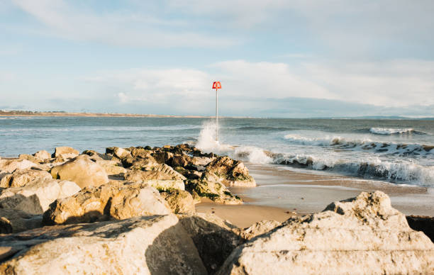 waves crashing against a light post on the coastline in Christchurch, England, United Kingdom