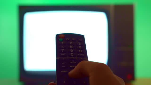 Person holding remote control and changing channels on vintage TV, old television on green background, blinking stripes and static noise on TV display. Changing channels and searching broadcasting on vintage television