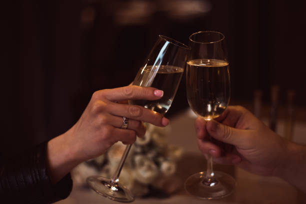 due bicchieri con champagne frizzante in mano, concetto per vacanza, bokeh, in un ristorante. cena romantica. un uomo e una donna tengono in mano bicchieri di champagne. concetto per san valentino o data. - champagne wedding luxury dinner foto e immagini stock