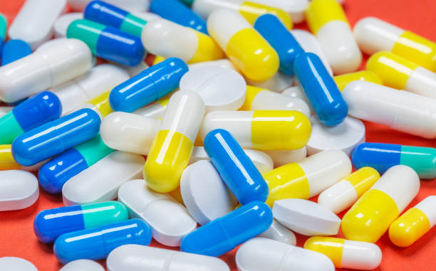 colored pills, pills and capsules on a red background - penicillin imagens e fotografias de stock
