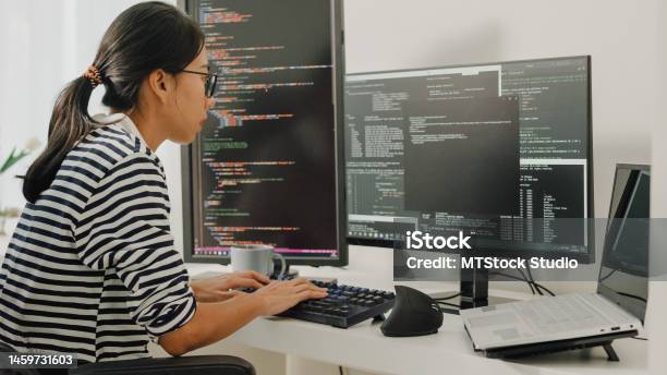 Young Asian Woman Software Developers Using Computer To Write Code Sitting At Desk With Multiple Screens Work Remotely At Home Stock Photo - Download Image Now