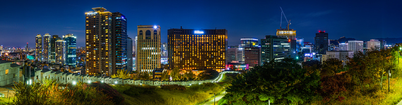 The glittering skycraper cityscape of central Seoul overlooking the spotlit battlements of the City Wall in the heart of South Korea’s vibrant capital city.