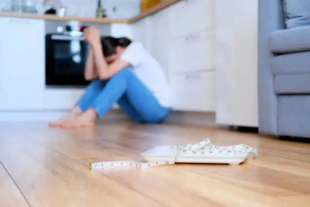 Photo of A woman in blue jeans sits on the floor and gets upset about her weight and body.