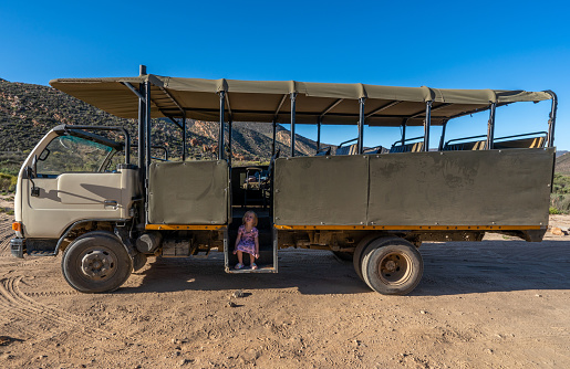 Toddler girl sitting on a safari vehicle with the beautiful rocky scenery east of Cape Town, South Africa.