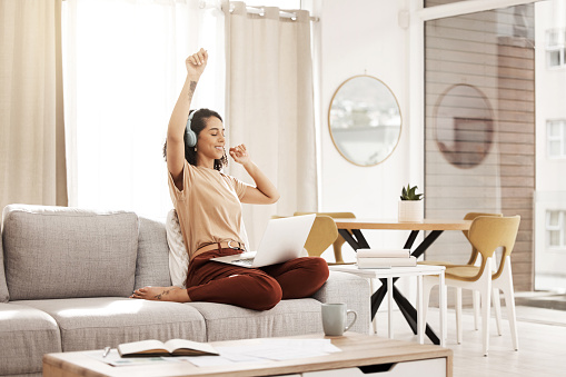 Music, laptop and woman dance on sofa while streaming audio podcast, radio sound or digital online playlist. Freedom, wellness and relax dancer girl with headphones listening to download song at home