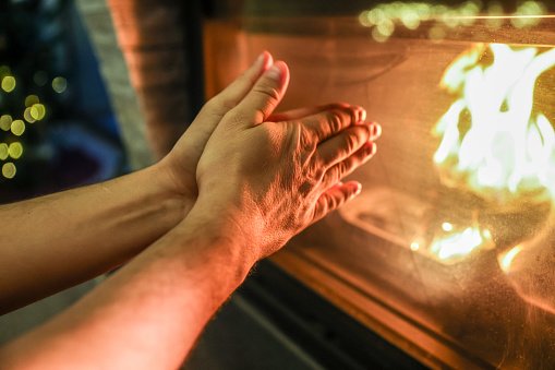 Man trying to keep warm, hands by the fireplace.