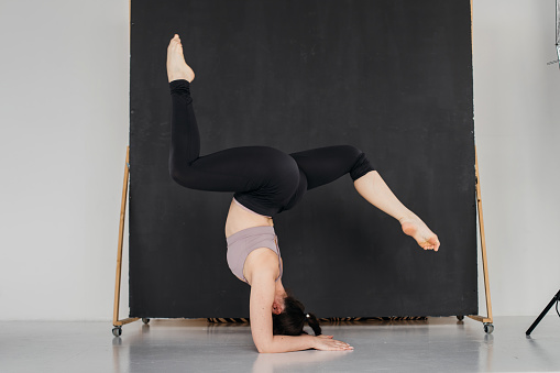 Young professional gymnast woman standing on splits. Pretty brunette girl doing an elbow stand. Female athlete doing warm-up before training. Copy space.