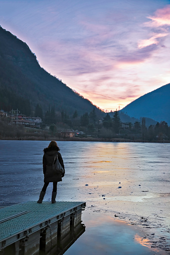 Girl admires the sunset on the shores of the frozen lake of Endine, in the province of Bergamo, Lombardy, Italy