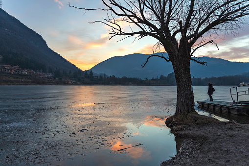 Girl on the shore of a frozen lake at sunset  in the backlight, land of Bergamo, Lombardy, Italy