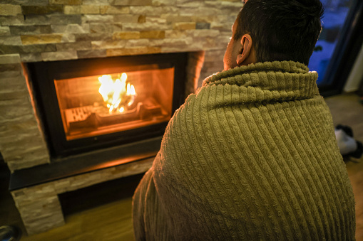 Back view of a man trying to keep warm by a fireplace.