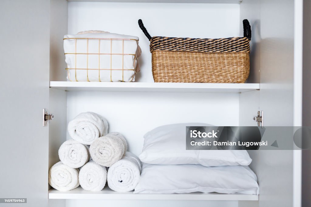 White laundry, pillows, towels organized and folded in baskets on shelves in white wardrobe. Space organization White laundry, pillows, towels organized and folded in baskets on shelves in white wardrobe. Space organization and storage system. Tidy up closet Organization Stock Photo