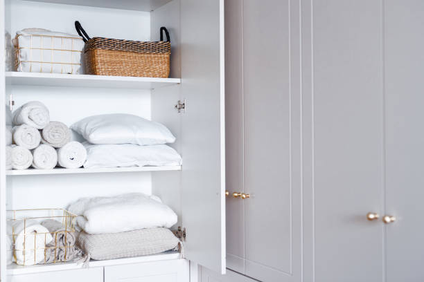 istock White laundry, pillows, towels organized and folded in baskets on shelves in white opened wardrobe. Clothes organization 1459755001