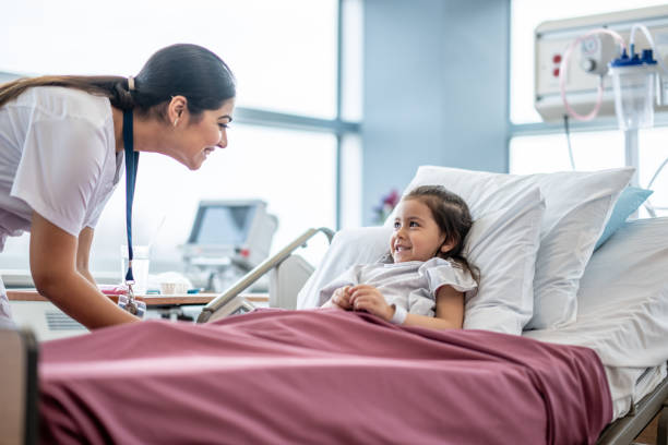 Nurse Checking on a Young Patient A female nurse of Middle Eastern decent leans in over the hospital bed of a little girl as she checks in on her after surgery. red medical scrubs stock pictures, royalty-free photos & images
