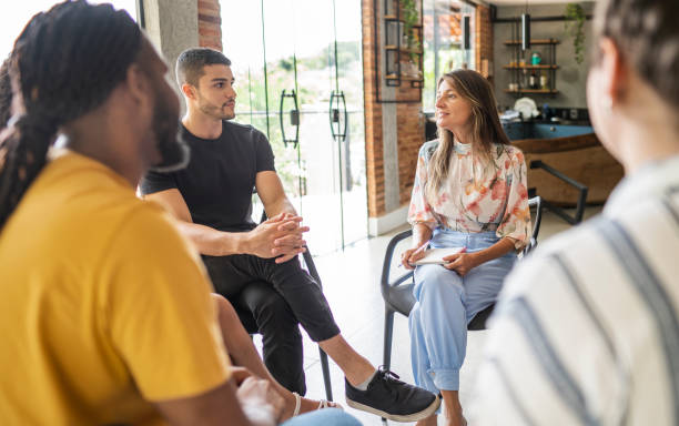 istock Smiling counselor talking during a group therapy session in her home 1459757154