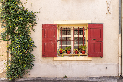 Aigues-Mortes, Gard, Occitania, France. Red shutters on a barred window in the south of France.