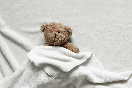 A brown teddy bear on a bed.
