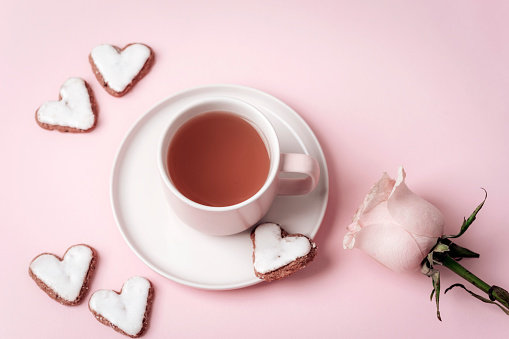 A cup of tea, heart-shaped cookies, pink rose on pink background. Valentines day concept. Top view.