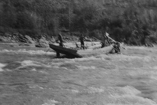 Group of men try to dislodge a scow boat that has run aground on the Athabasca River in Alberta, Canada. Vintage photograph ca. 1915.